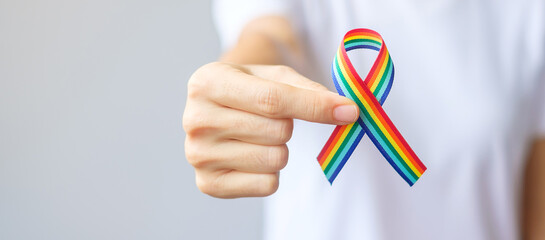 hand holding LGBTQ Rainbow ribbon for Support Lesbian, Gay, Bisexual, Transgender and Queer community and Pride month concept