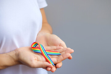 hand holding LGBTQ Rainbow ribbon for Support Lesbian, Gay, Bisexual, Transgender and Queer community and Pride month concept