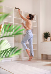 Young barefoot woman taking book from shelf at home