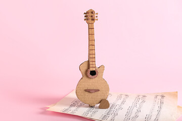 Cardboard guitar with note sheets on pink background