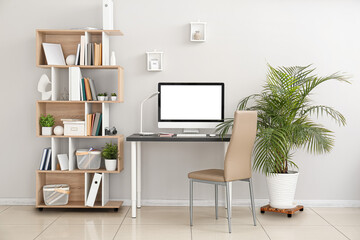 Interior of light office with workplace, houseplants and shelving unit