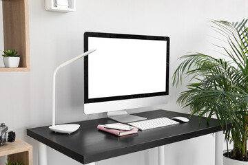 Workplace with computer, lamp and notebook near light wall