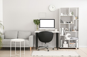 Interior of light office with workplace, shelving unit and sofa
