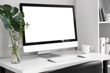 Workplace with computer, plant branches in vase and cup near light wall