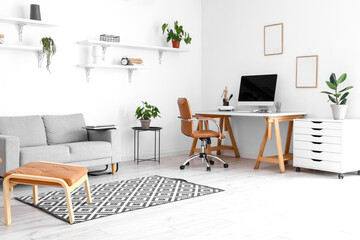 Comfortable sofa and workplace with modern computer near white wall in room interior