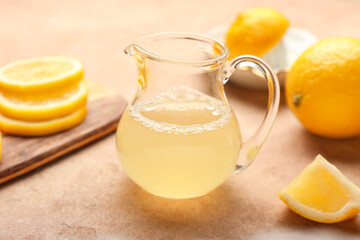 Jug of fresh lemon juice on color background