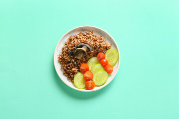 Plate of tasty buckwheat porridge with mushrooms and vegetables on turquoise background, top view