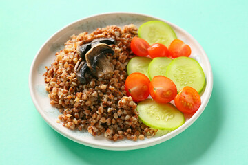 Plate of tasty buckwheat porridge with mushrooms and vegetables on turquoise background