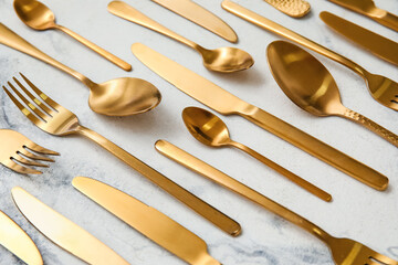 Many different golden cutlery on light marble background