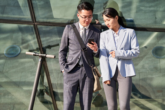 young asian businessman and businesswoman looking at cellphone together outdoors