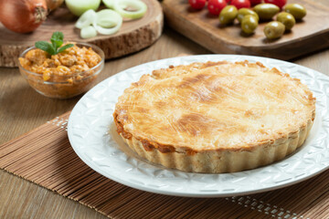 Chicken pie with cottage cheese, tomatoes, onion and olives on wooden table and white plate.