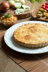 Chicken pie with cottage cheese, tomatoes, onion and olives on wooden table and white plate.