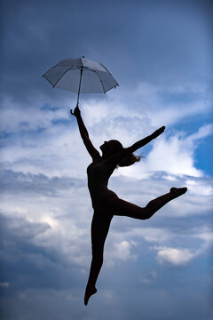 Silhouette of woman with umbrella doing stretching up exercise outdoors. Dance studio.