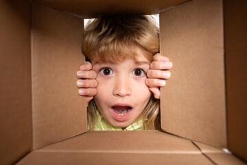 Unpacking cardboard box for kids. Cheerful cute child opening a present. View from inside of the box. Closeup kids face.