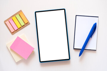 Tablet with copy space, mockup on light beige background. Stationery, stickers, notebook, blue pen around. Minimalism, flat lay, top view.