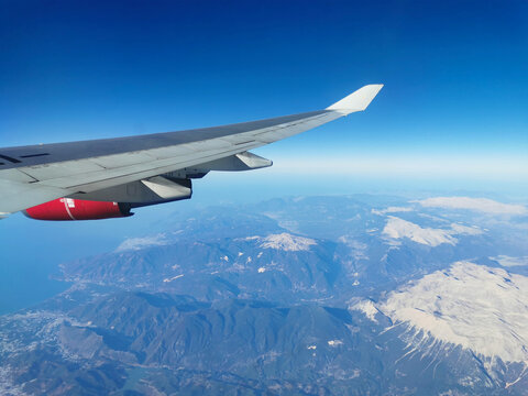 View from the porthole on the wing of an airplane with a red aircraft engine flying to Cyprus in the morning over beautiful mountains with snowy peaks.