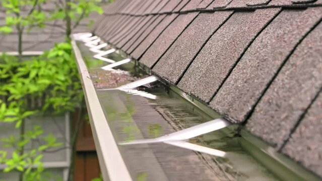 Rain water overflowing a gutter on a home with roof.