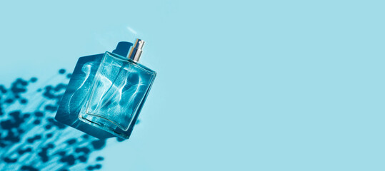 Transparent bottle of perfume on a blue background. Fragrance presentation with daylight. Trending concept in natural materials with plant shadow. Women's and men's essence. - obrazy, fototapety, plakaty