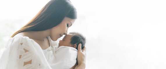 Panoramic banner image of beautiful young Asian mother kissing and hugging newborn baby. Beautiful...