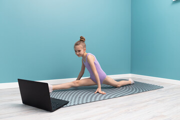 A young girl is doing gymnastics in front of a laptop. Classes at home