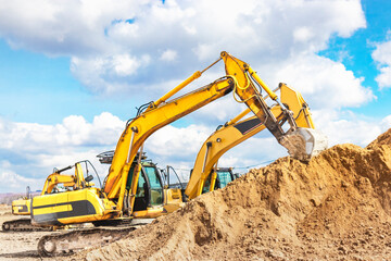 Fototapeta na wymiar Two powerful excavators work at the same time on a construction site, sunny blue sky in the background. Construction equipment for earthworks.