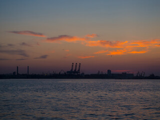 Beautiful sunset above port with silhouettes of cargo cranes. Industrial black sea port Odesa, Ukraine with a lot of cranes, cabins, boxes and tanks by the water at evening dusk