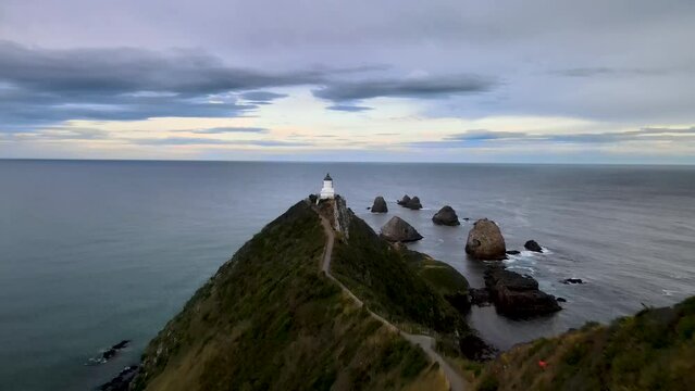 Drone flying to Nugget Point Lighthouse, popular scenic point in New Zealand. Girl is looking from viewing platform to horizon.