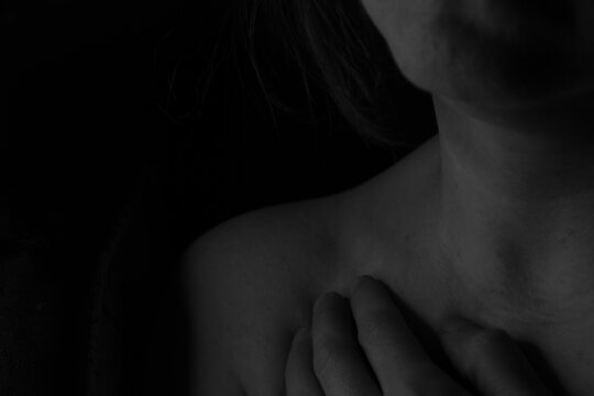 The girl on a dark background put her hand to her chest. Photo in low key. Black and white photo. Close-up.