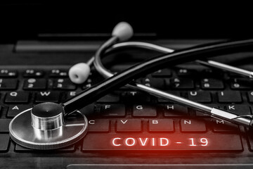 A stethoscope placed near the "Covid 19" button has a red alert light on a laptop computer.