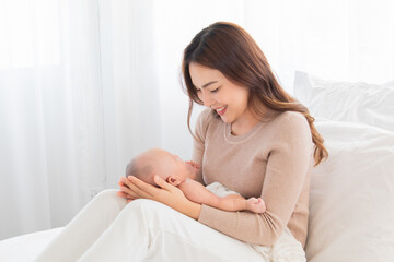 Selective focus Beautiful Asian mother supports and tenderly cuddles newborn baby gently while infant lying on lap. Mom looking and lift baby with love and care. Toddler deeply sleeping on woman lap.