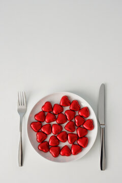 Love, romance and Valentine's day concept - plate with red hearts, fork, knife and copy space over white table