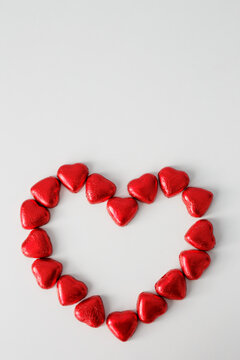 frame of chocolate hearts in red foil in the shape of a heart and copy space over white