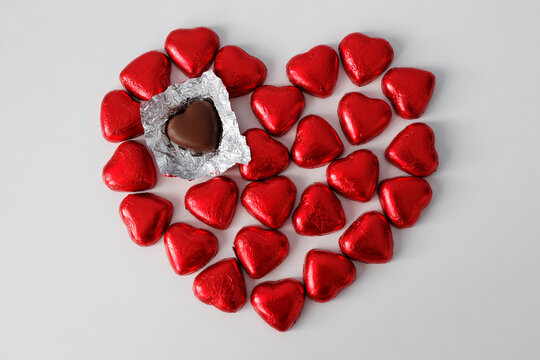 Love and broken haert concept - heart shape chocolate candies wrapped in red foil over white