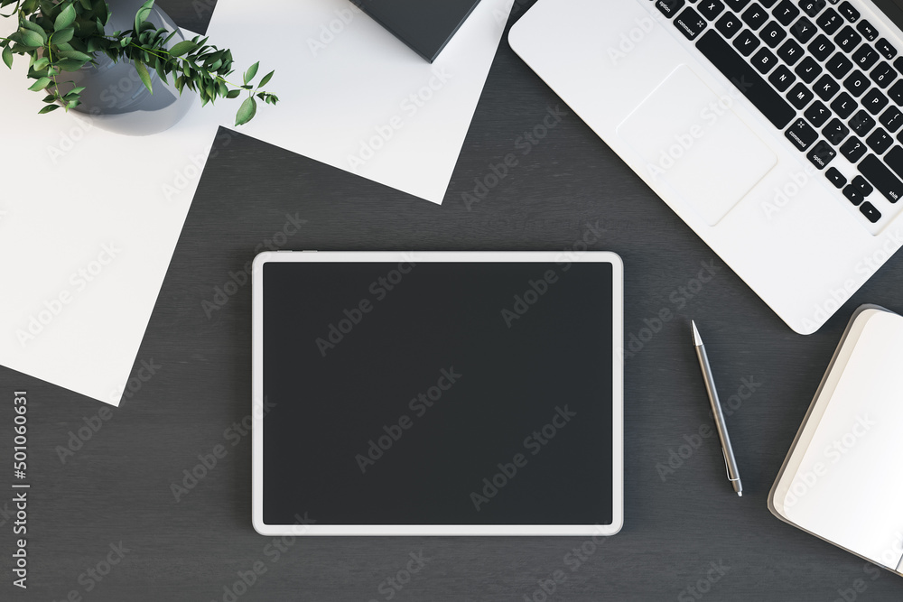 Poster tablet with blank screen is on top of dark wooden office desk table with laptop computer and supplie