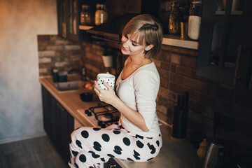 Young beautiful woman wearing pajamas drinking tea on the kitchen.