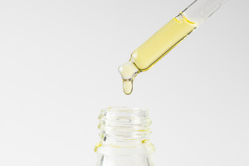 Transparent pipette with cosmetic liquid on a white background. Essential oil dropper close up