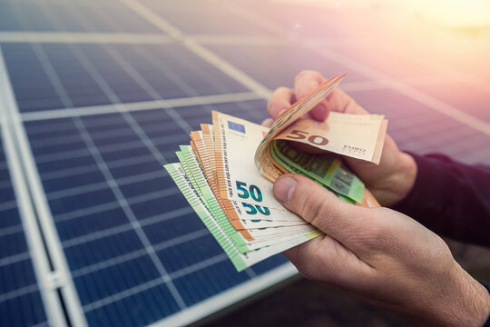 beautiful young hands in black hold a sum of euros in front of solar panels.