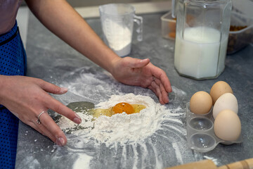 Beautiful young female hands break eggs into flour to knead a beautiful dough.