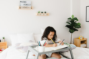 Little kid girl hands detail drawing intently with multicolored pencils in bedroom at home. on white background. Copy space for text.