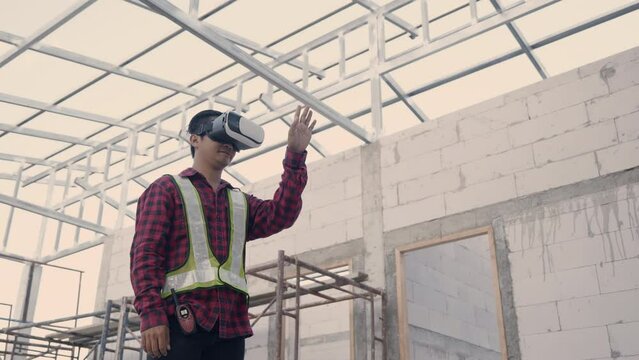 Asian architect engineer worker man in protective helmet and uniform using VR gear glasses to visualize planning and development projects while working at the house building construction site