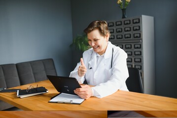 Portrait of female doctor counseling patient via video call. Professional physician in white lab...