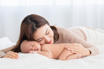 Obraz na płótnie Canvas Beautiful asian mom supports and tenderly cuddles newborn baby gently while baby sleeping. Young woman kissing and touching on back child with love and tender. Mother and infant spend time together.