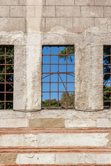 Three trellised windows in block wall with blue sky on other side. Vertical photo.