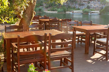 Wooden empty tables with massive chairs in restaurant on river bank.