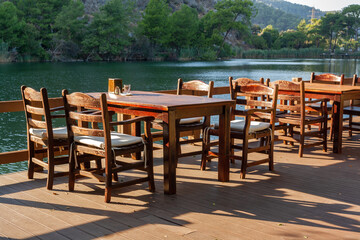 Wooden empty tables with chairs in restaurant on river bank. Horizontal photo.