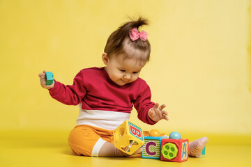 Girl 1 year old, playing with educational cubes with the English alphabet. The girl is sitting on the floor on a yellow background.
