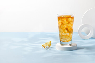 Delicious refreshing summer drink, iced tea in a glass on podium. Sunshine, blue background. Copy...