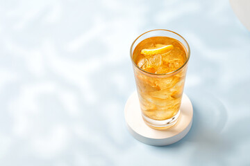 Refreshing lemonade in sunny day. Iced cold tea with lemon in highball on blue background