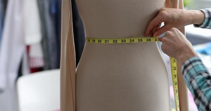 Designer stylist measures waist with centimeter on mannequin