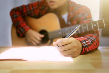 Asian man in a plaid shirt is writing his idea in the notebook paper and in his arm have the...